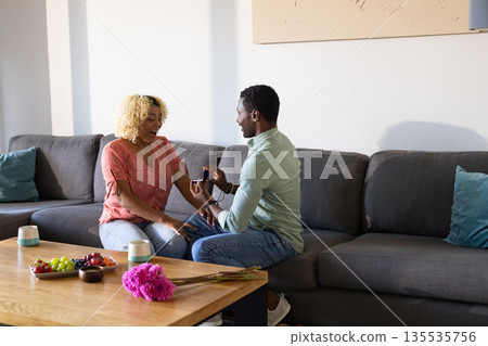African American man proposing to woman on sofa at home, both looking happy African American man proposing to woman on sofa at home, both looking happy 135535756