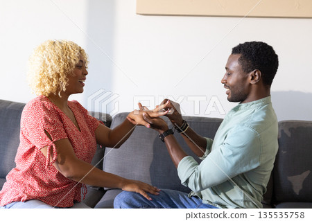 Exchanging rings on couch, African American couple smiling, cherishing moment together 135535758