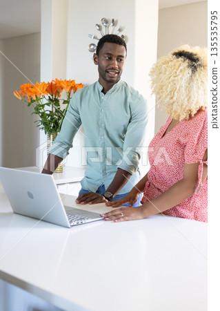 Friends collaborating on laptop in modern kitchen, discussing project ideas 135535795