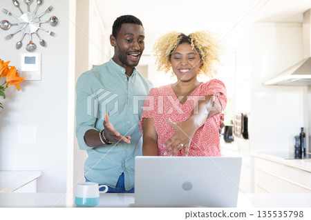 Friends happily video chatting on laptop in bright kitchen, enjoying conversation Friends happily video chatting on laptop in bright kitchen, enjoying conversation 135535798