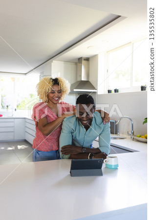 Smiling friends watching tablet together in modern kitchen, enjoying leisure time Smiling friends watching tablet together in modern kitchen, enjoying leisure time 135535802