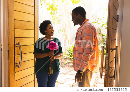 Woman holding flowers smiling at man standing in doorway at home Woman holding flowers smiling at man standing in doorway at home 135535835
