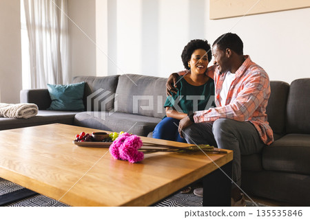 African American couple sitting on sofa at home, laughing and enjoying conversation African American couple sitting on sofa at home, laughing and enjoying conversation 135535846