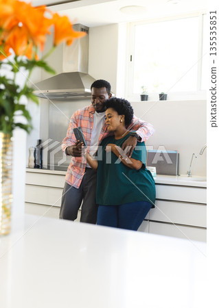 In kitchen, African American couple looking at smartphone, smiling together 135535851