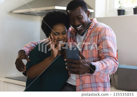 African American couple smiling and video chatting on smartphone in kitchen 135535855