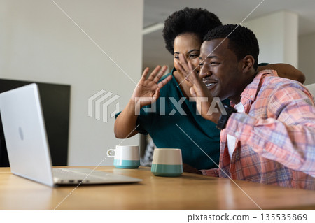 African American friends video chatting on laptop at home, smiling and waving 135535869