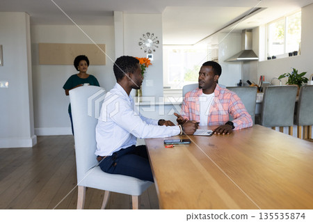 Two men discussing business at home while woman observes in background 135535874