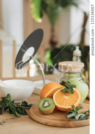 A collection of vibrant fruits including oranges, kiwi, and apples, alongside fresh mint leaves, are arranged on a wooden cutting board, ready for juicing or a healthy meal 135536007