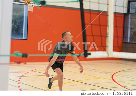 Mid adult man in sportswear crouching on gym court next to volleyball net, copy space Mid adult man in sportswear crouching on gym court next to volleyball net, copy space 135536111