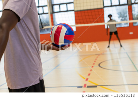 African american male teammates practicing in shorts on court holding ball next to net, copy space 135536118