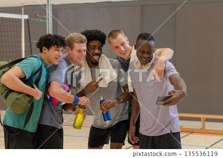 Diverse male friends posing for selfie on volleyball court with smartphone, volleyball 135536119