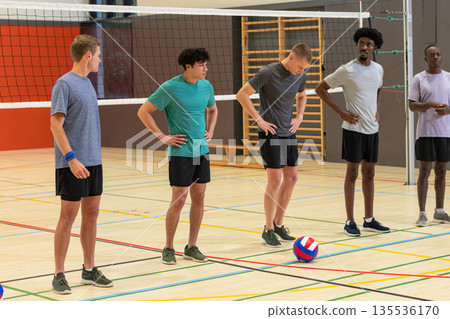 Diverse male volleyball team standing on court with boundary lines, net, volleyball, sneakers Diverse male volleyball team standing on court with boundary lines, net, volleyball, sneakers 135536170