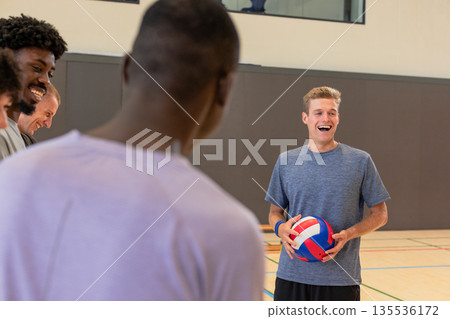 Male volleyball team watching coach holding volleyball showing serve on court, copy space Male volleyball team watching coach holding volleyball showing serve on court, copy space 135536172