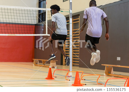 African american men jumping over hurdles at sports hall, volleyball net, cones African american men jumping over hurdles at sports hall, volleyball net, cones 135536175