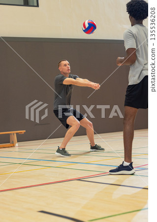 Diverse male teammates executing forearm bump on gym court with volleyball, bench, copy space Diverse male teammates executing forearm bump on gym court with volleyball, bench, copy space 135536208