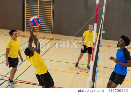 African american man jumping overhead pushing red, white, blue volleyball past net at gym African american man jumping overhead pushing red, white, blue volleyball past net at gym 135536223