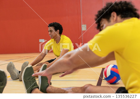 African american partners stretching legs on gym floor with volleyball, cones, copy space 135536227