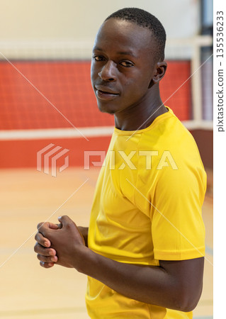 African american male athlete standing beside volleyball net on gym court in yellow jersey 135536233