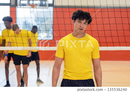 Diverse male volleyball partners in yellow shirts practicing strategy behind net on polished court Diverse male volleyball partners in yellow shirts practicing strategy behind net on polished court 135536240