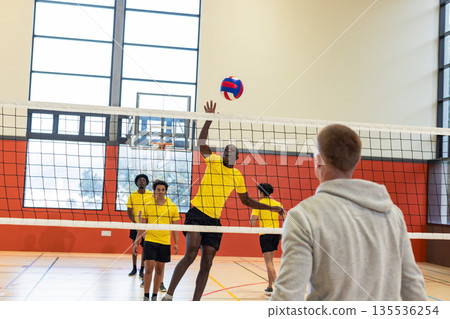 Volleyball team practicing spiking red-blue volleyball over net at gym in yellow jerseys Volleyball team practicing spiking red-blue volleyball over net at gym in yellow jerseys 135536254