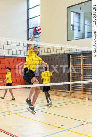Diverse male teammates jumping at net, spiking red-white-blue volleyball on polished court 135536261