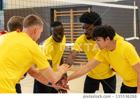 Diverse male volleyball teammates huddling and stacking hands on court with net, boundary lines Diverse male volleyball teammates huddling and stacking hands on court with net, boundary lines 135536268