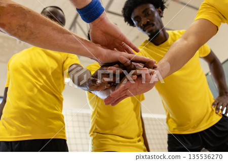 Diverse male athletes stacking hands in huddle at gym court wearing yellow jerseys, black shorts Diverse male athletes stacking hands in huddle at gym court wearing yellow jerseys, black shorts 135536270