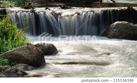 Tranquil Waterfall Flowing Gently Over Rocks Surrounded by Lush Greenery in a Serene Natural Landscape During Daylight Hours 135536386