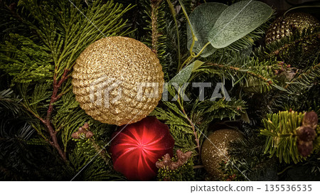 festive arrangement of glittering colorful Christmas ornament balls nestled in lush evergreen branches, creating a warm, celebratory mood perfect for holiday decor and seasonal stock photography 135536535