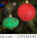 festive arrangement of glittering colorful Christmas ornament balls nestled in lush evergreen branches, creating a warm, celebratory mood perfect for holiday decor and seasonal stock photography 135536549