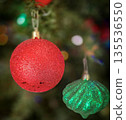 festive arrangement of glittering colorful Christmas ornament balls nestled in lush evergreen branches, creating a warm, celebratory mood perfect for holiday decor and seasonal stock photography 135536550