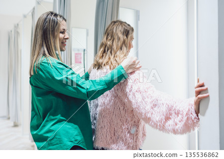 Two women shopping in store trying on clothes in fitting room 135536862