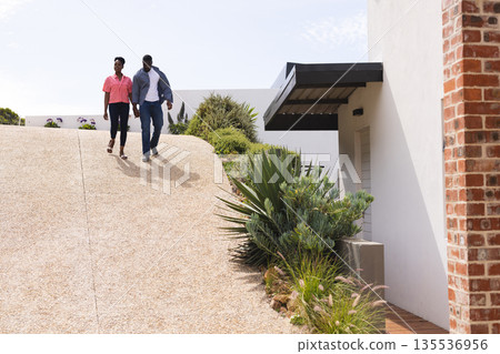 Couple walking down driveway, enjoying sunny day outside modern home 135536956