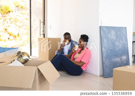 Couple enjoying coffee break while unpacking boxes in new home, feeling relaxed Couple enjoying coffee break while unpacking boxes in new home, feeling relaxed 135536959