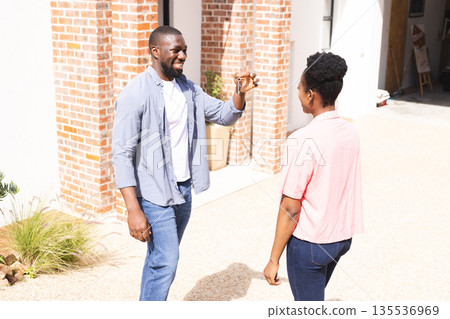 Man joyfully presenting house keys to woman outdoors, celebrating new home purchase Man joyfully presenting house keys to woman outdoors, celebrating new home purchase 135536969