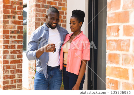 Couple celebrating new home, smiling and holding keys outside brick house 135536985