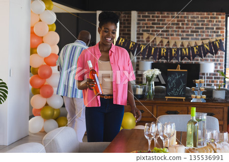 Smiling woman holding wine bottle at retirement party with festive decorations Smiling woman holding wine bottle at retirement party with festive decorations 135536991