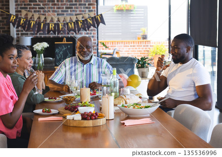 Family celebrating retirement with food and drinks at home, enjoying togetherness Family celebrating retirement with food and drinks at home, enjoying togetherness 135536996