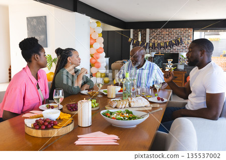 Family celebrating retirement with food and drinks, enjoying conversation at home Family celebrating retirement with food and drinks, enjoying conversation at home 135537002