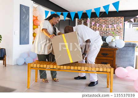 Couple joyfully opening large gift box during festive celebration at home Couple joyfully opening large gift box during festive celebration at home 135537039