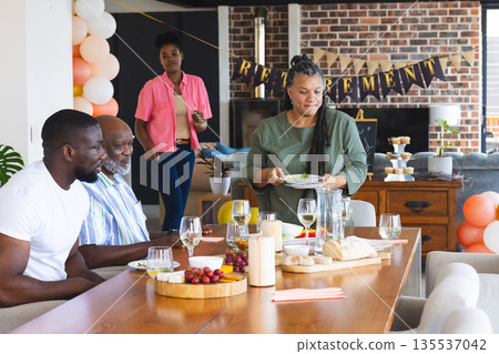 Family celebrating retirement party at home, enjoying food and drinks together 135537042