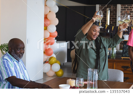 Joyful woman raising wine glasses in celebration at home with friends Joyful woman raising wine glasses in celebration at home with friends 135537043