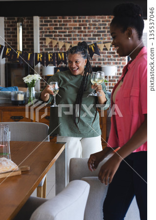 Joyful woman holding wine glasses celebrating retirement at home with friends Joyful woman holding wine glasses celebrating retirement at home with friends 135537046