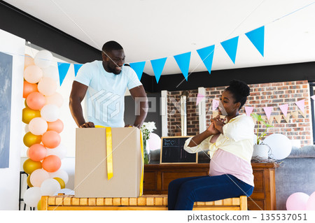 Expectant couple celebrating baby shower with gift box and colorful decorations 135537051