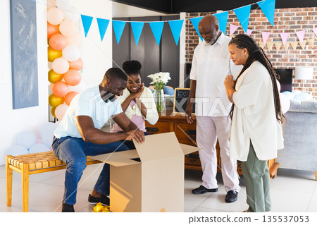 Family celebrating together as man opens gift box in decorated living room Family celebrating together as man opens gift box in decorated living room 135537053