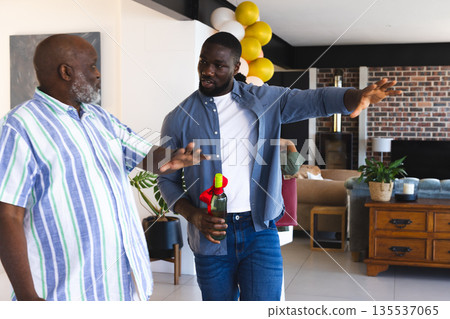 Two men in casual attire discussing while holding wine bottle at home Two men in casual attire discussing while holding wine bottle at home 135537065