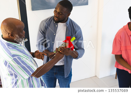 Man giving gift bottle to smiling older man at home celebration gathering 135537089