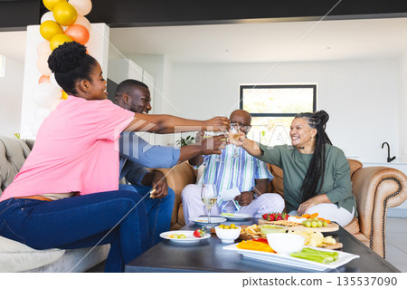 Friends toasting with drinks at home, celebrating with snacks and laughter Friends toasting with drinks at home, celebrating with snacks and laughter 135537090