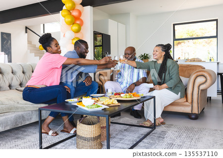 Family celebrating at home, toasting with drinks and enjoying snacks together Family celebrating at home, toasting with drinks and enjoying snacks together 135537110