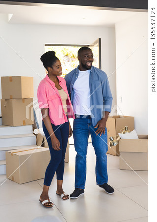 Couple standing in new home surrounded by moving boxes, smiling and excited Couple standing in new home surrounded by moving boxes, smiling and excited 135537123